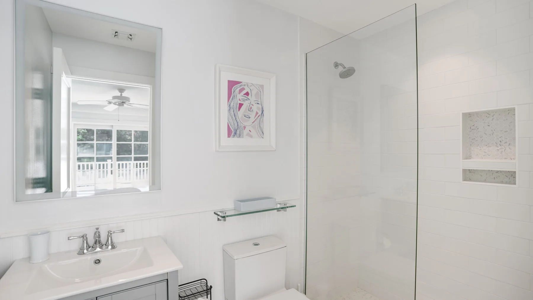 Un baño luminoso con lavabo, espejo de pared y ducha de vidrio.