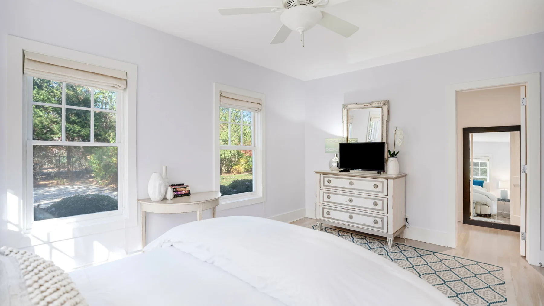 Un dormitorio luminoso con cama, cómoda y ventanas con vistas a la vegetación.