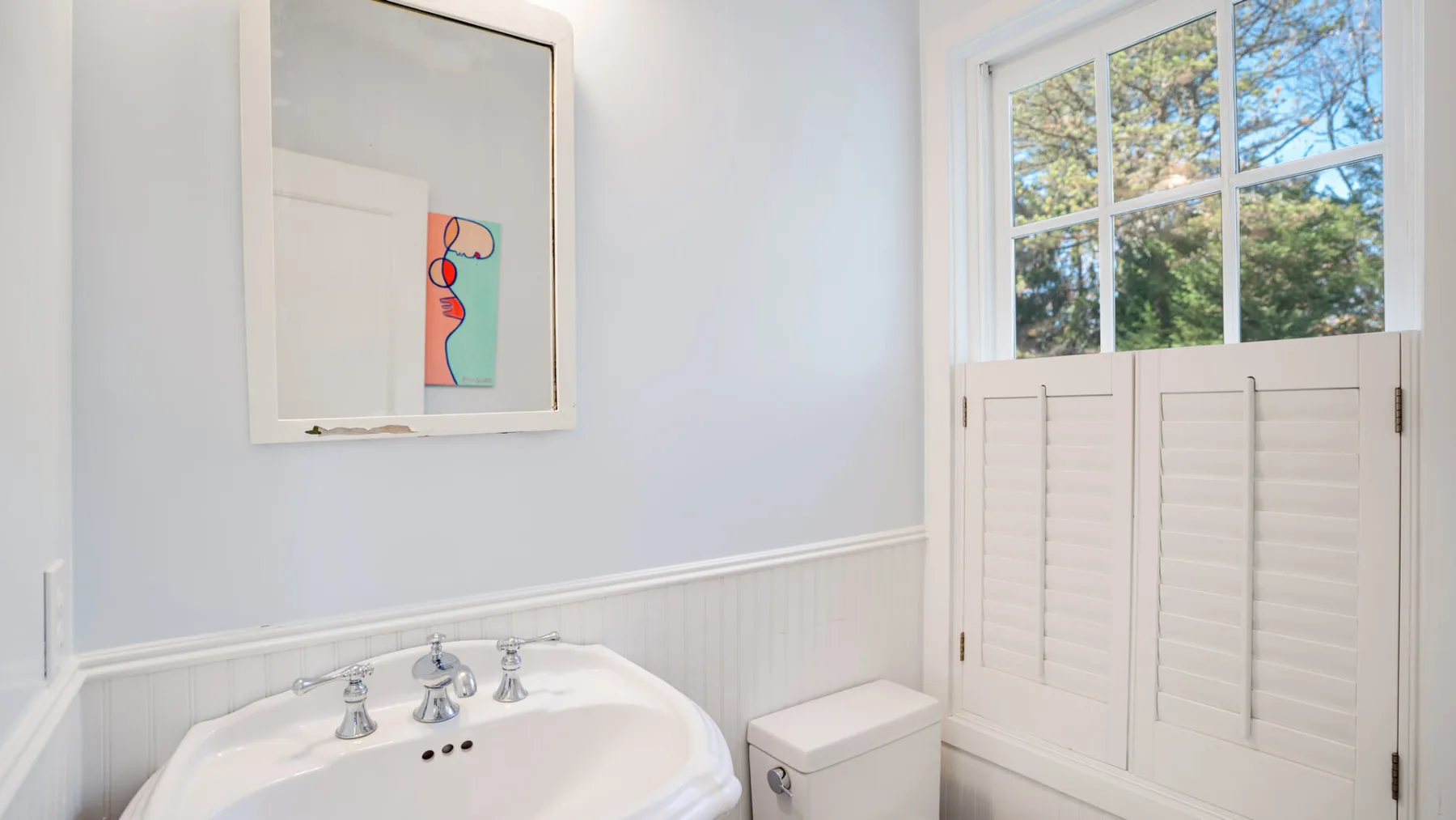 Un baño con lavabo, inodoro y contraventanas en la ventana.