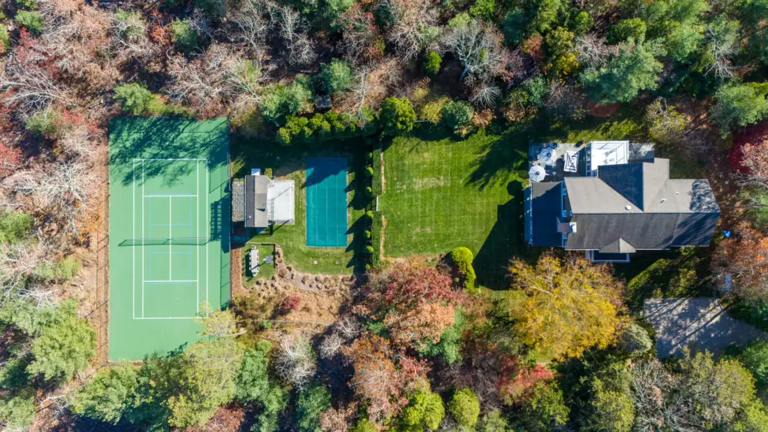 Una vista aérea muestra una casa junto a una cancha de tenis y jardines.