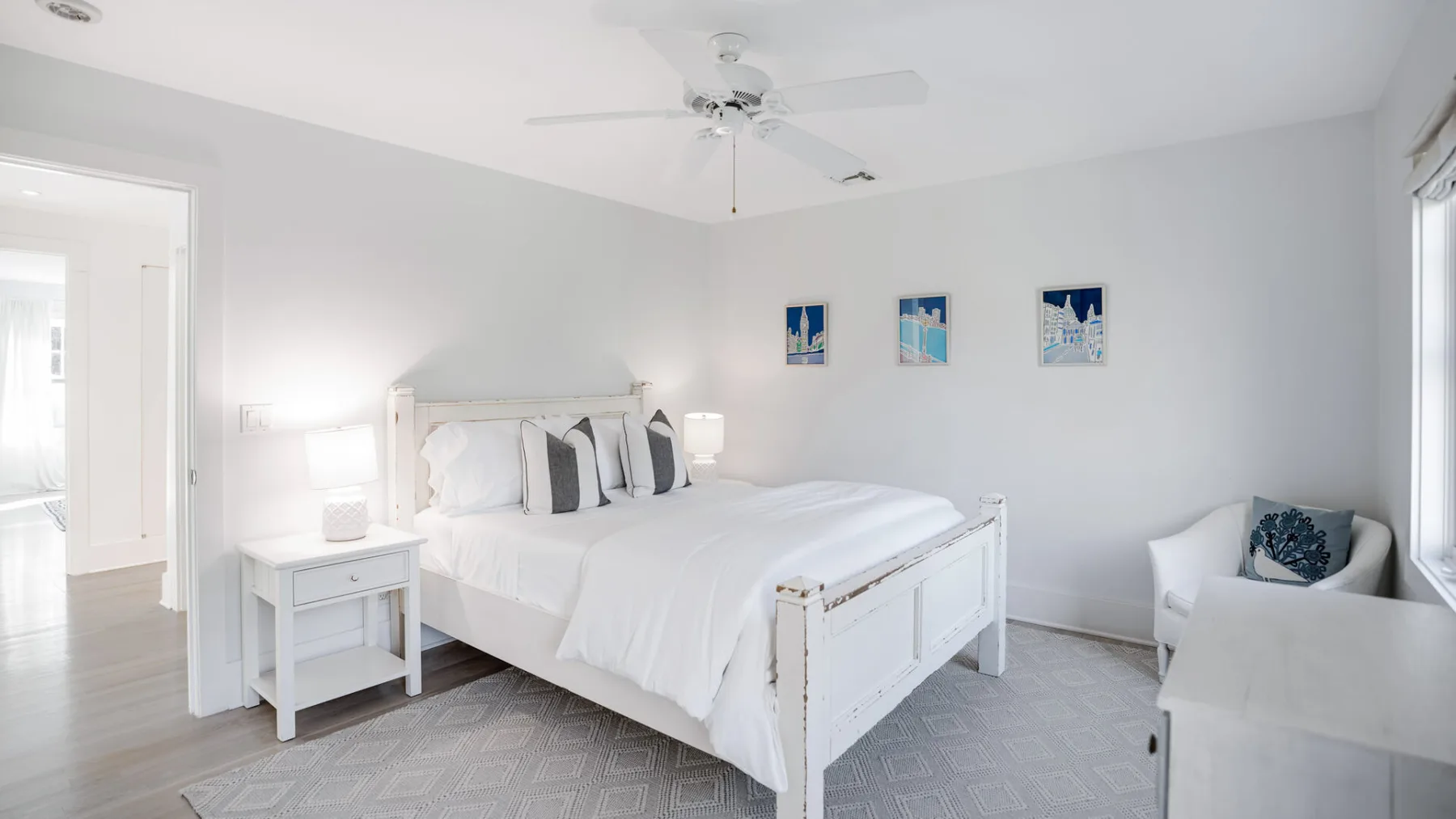 Un dormitorio luminoso con una cama blanca y cuadros en la pared.