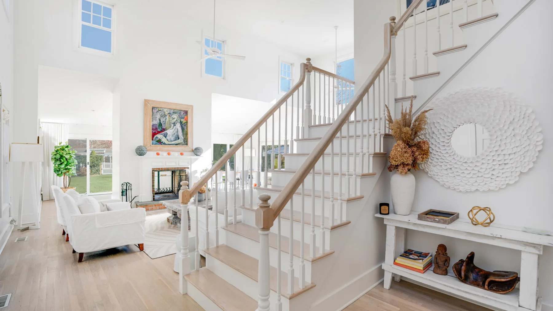 Una luminosa sala de estar da a una escalera, con asientos blancos y una chimenea.