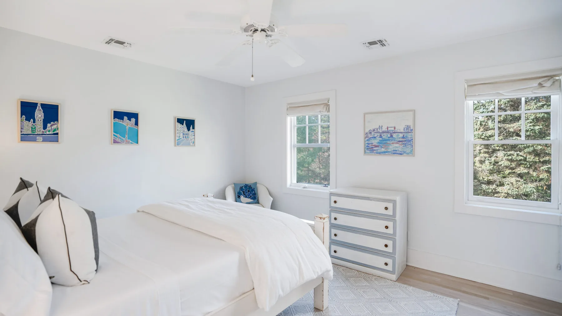 Un dormitorio luminoso con dos camas y una cómoda junto a las ventanas.