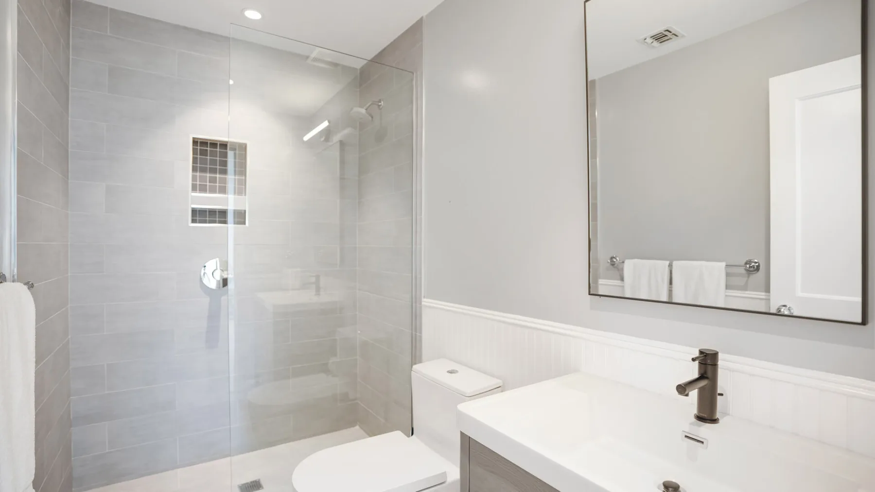 Un baño luminoso con ducha de vidrio y un tocador blanco.