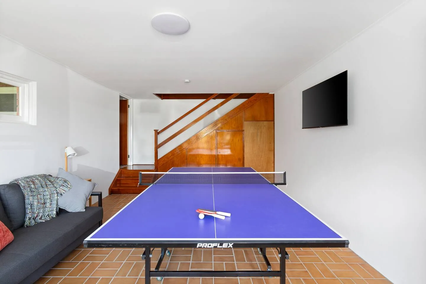A ping-pong table fills a bright living room with a staircase and seating.