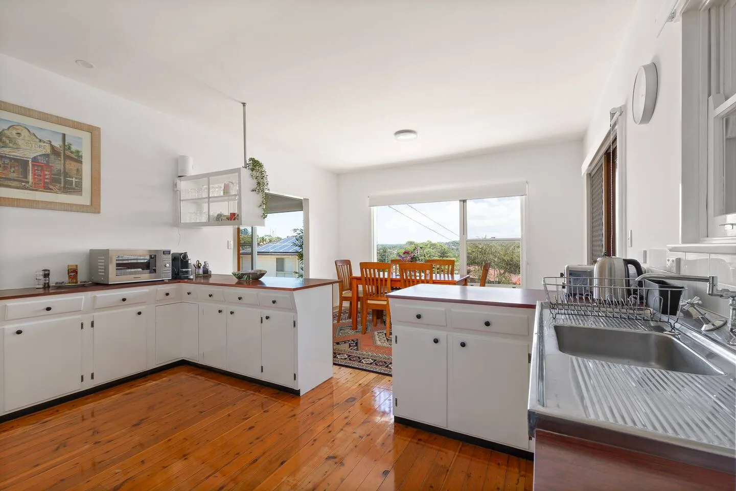 A bright kitchen with white cabinets opens onto a dining area by the windows.