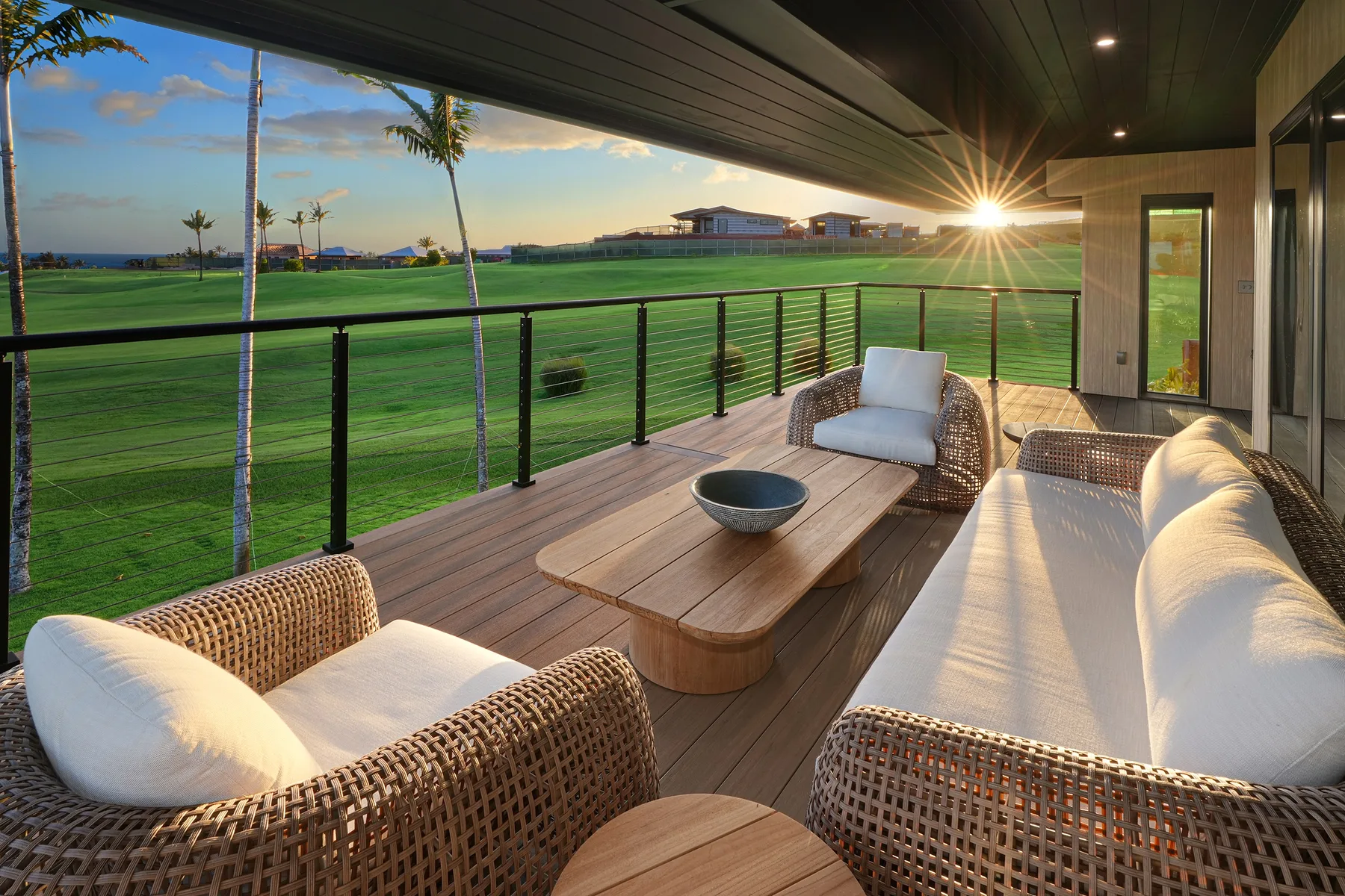 Una zona de estar exterior cubierta tiene vistas a un paisaje verde al atardecer.