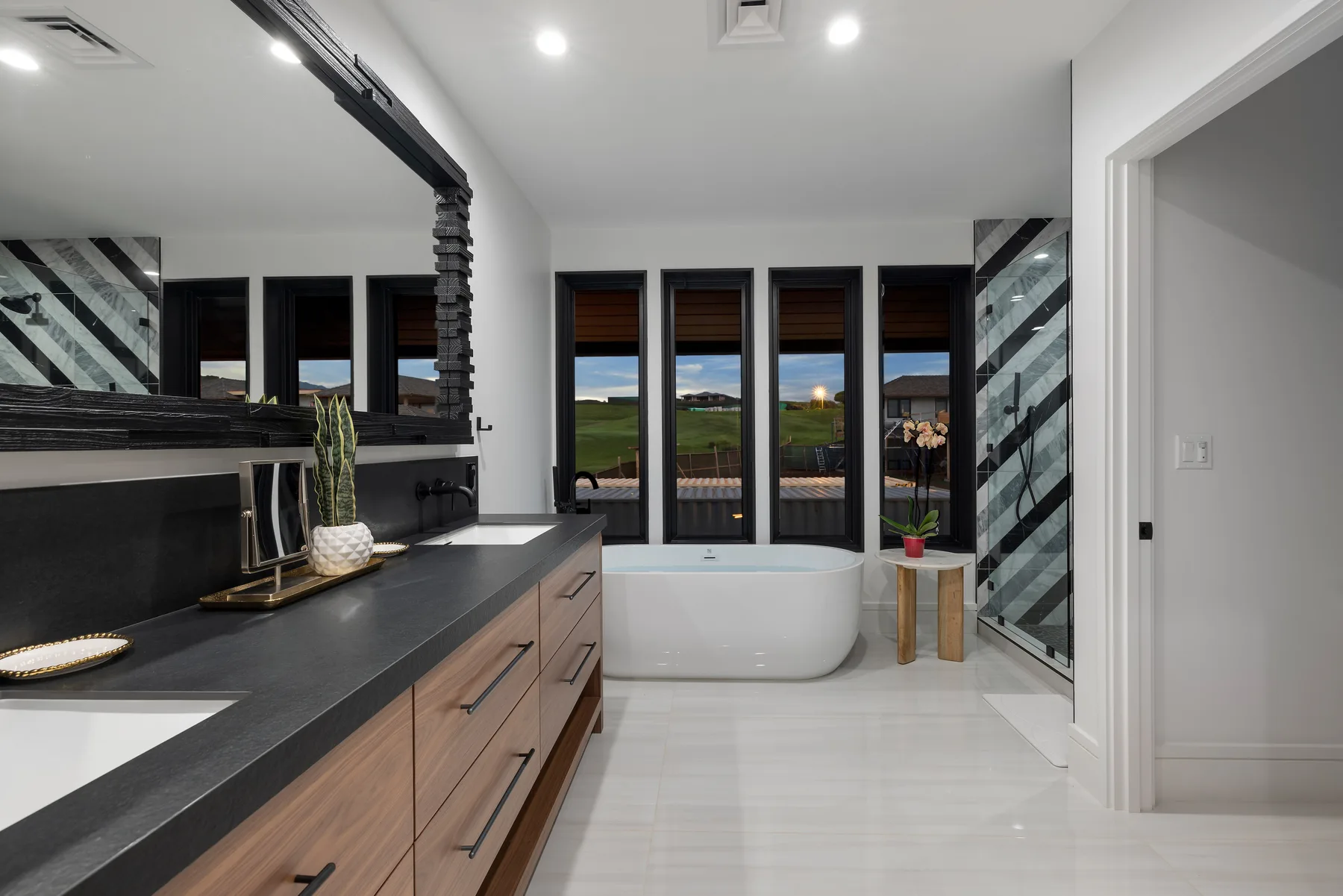 Un baño moderno con bañera, tocador oscuro y ventanas con vistas a un paisaje verde.