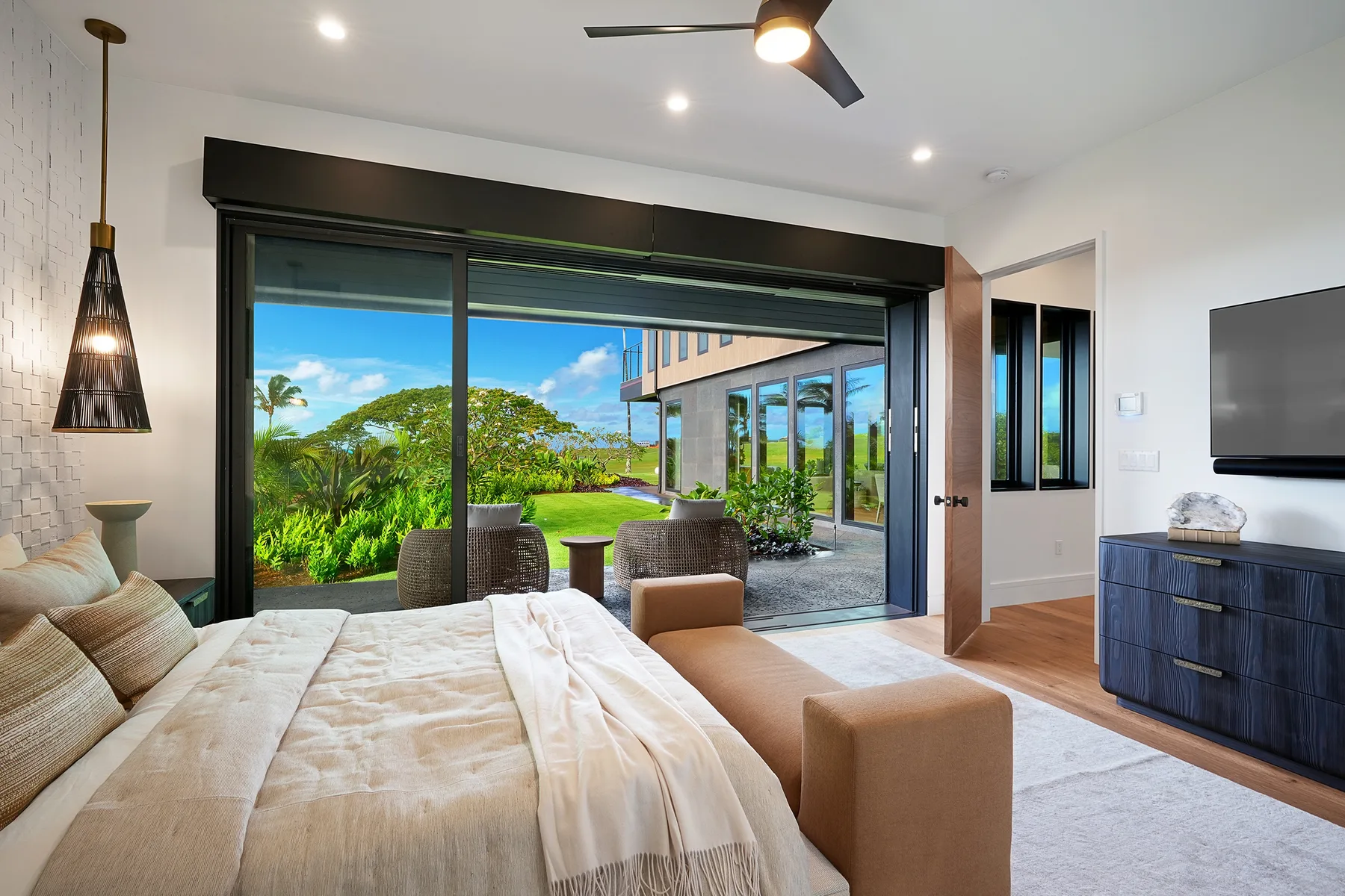 Un dormitorio luminoso con una cama frente a grandes puertas de vidrio y vistas al jardín.