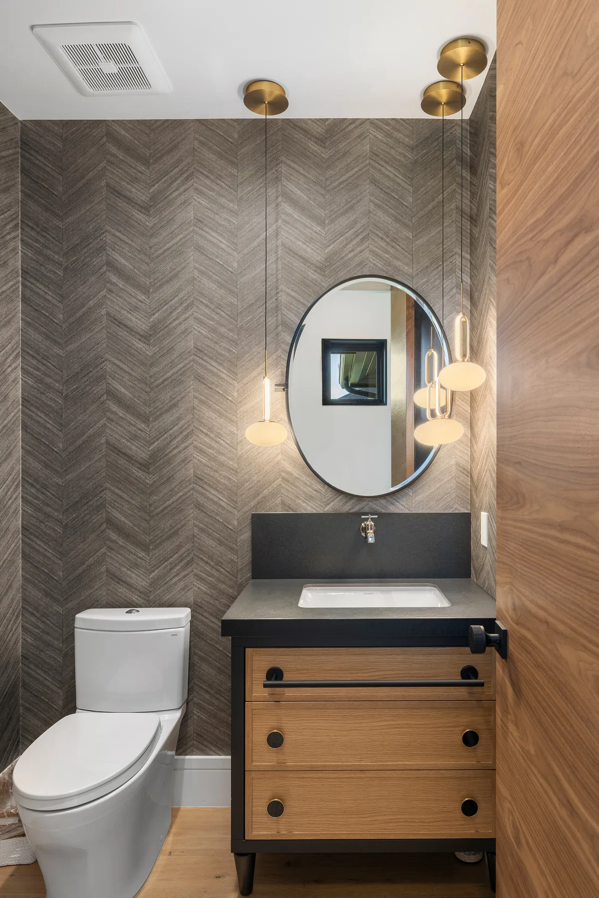 Un baño con un mueble de madera, inodoro y espejo ovalado.