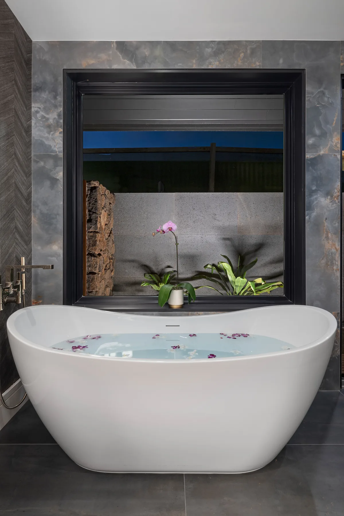 Un baño moderno tiene una bañera exenta bajo una ventana grande.