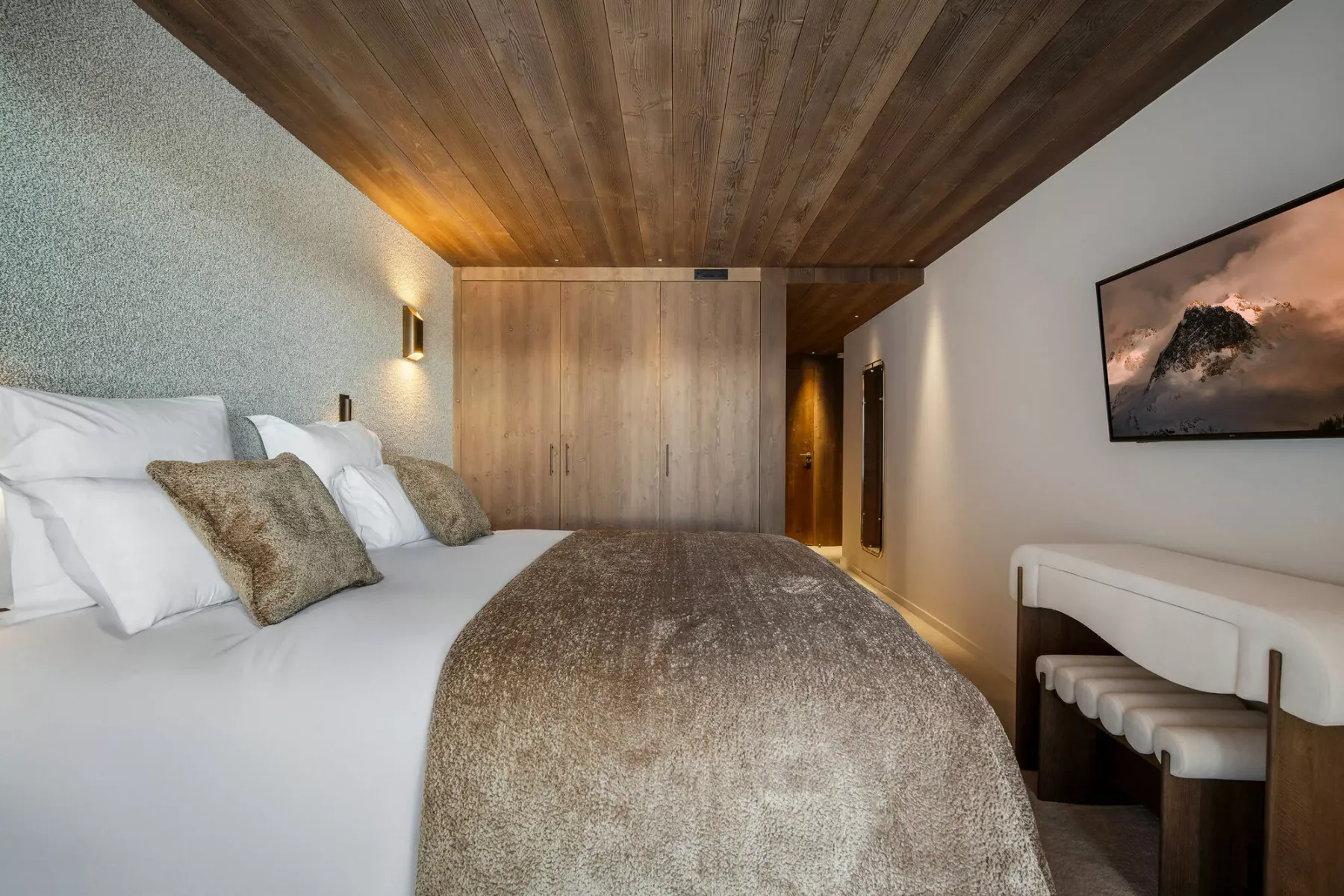 A bedroom with a bed, a wooden wardrobe, and a framed mountain picture.