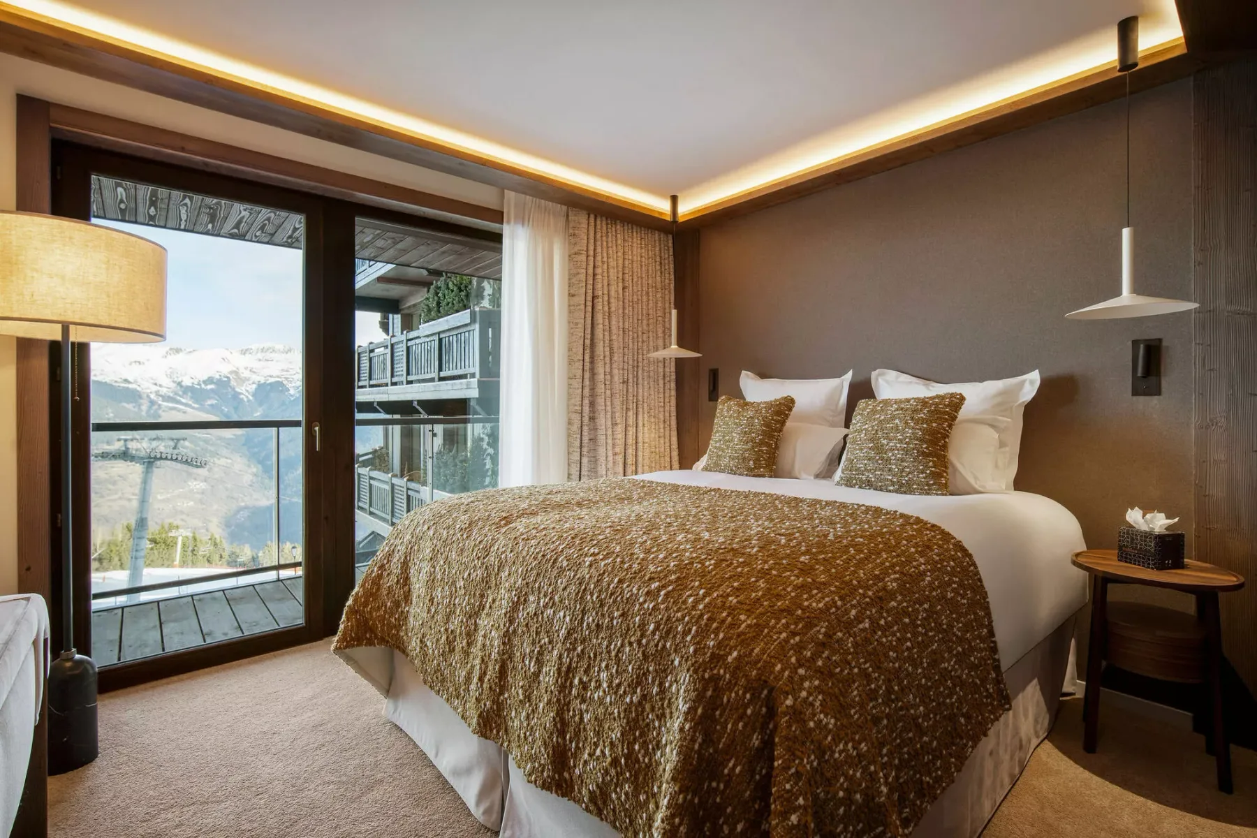 A bedroom with a bed, bedside table, and windows overlooking the mountains.