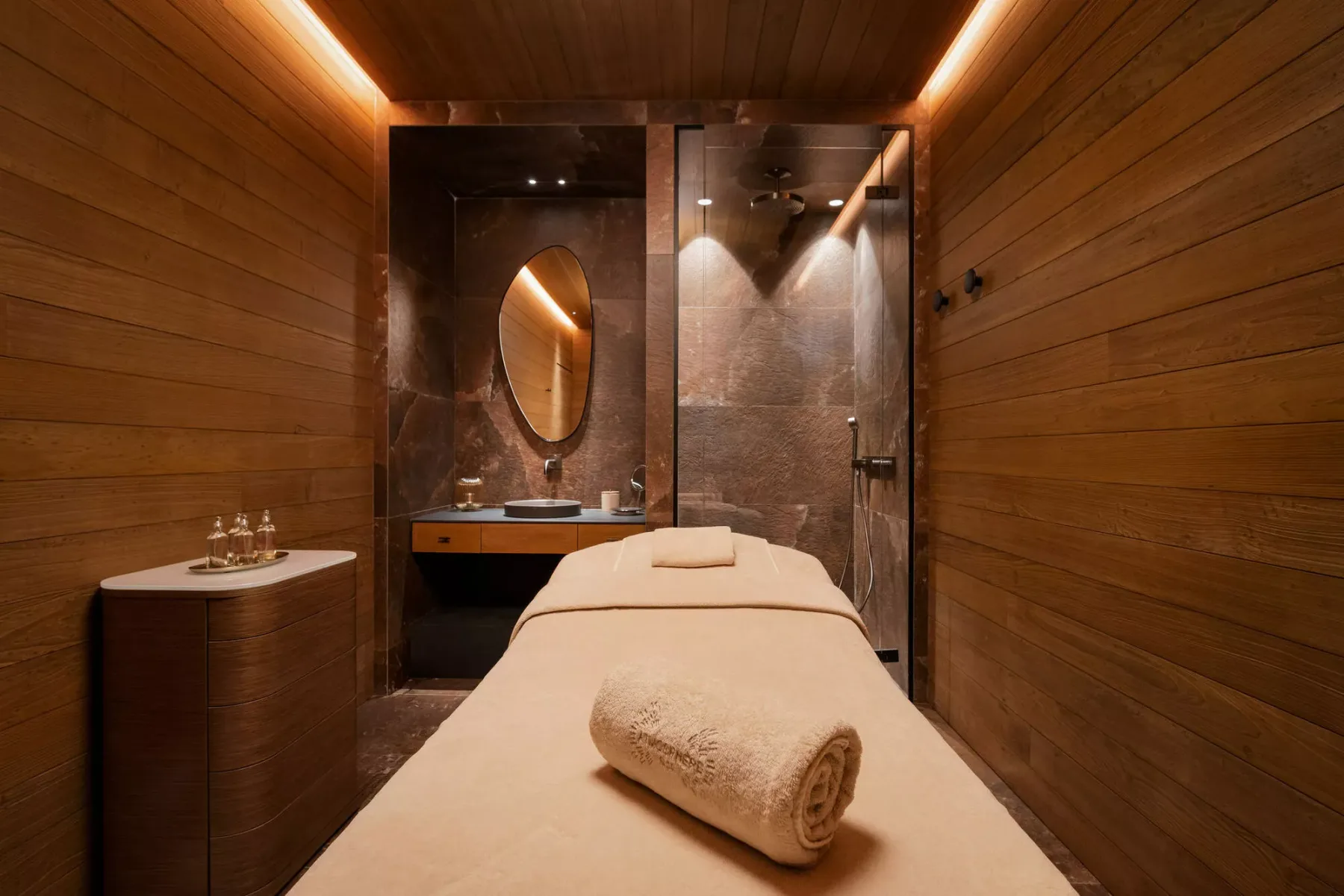 A massage room with a treatment table and a sink beneath a lit mirror.