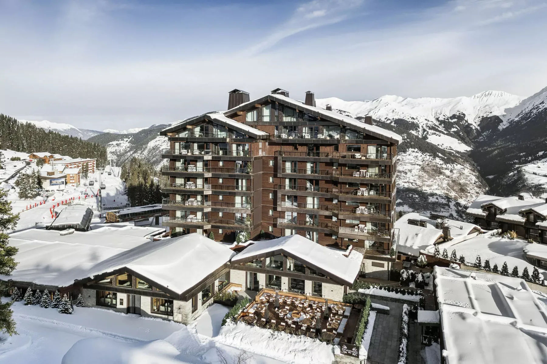 A large apartment building stands among snow-covered mountain slopes.
