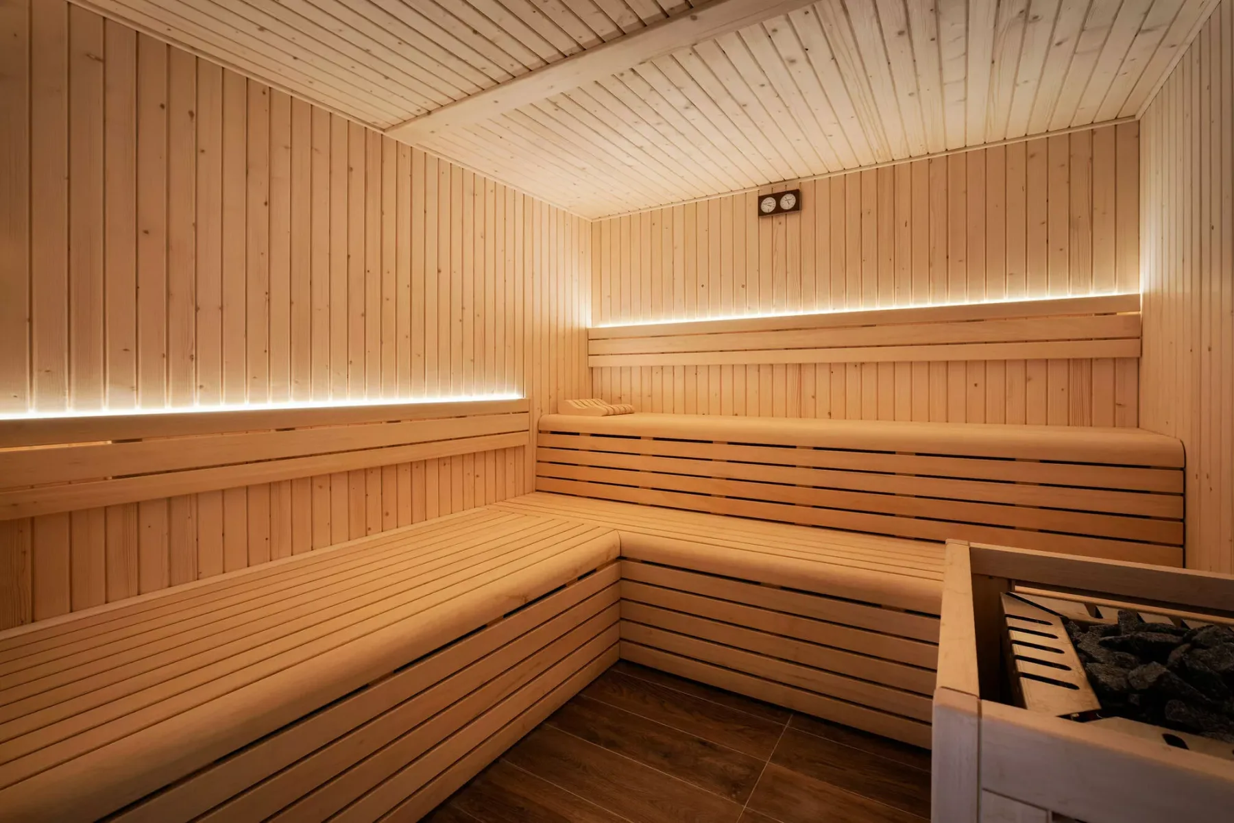 A wood-paneled sauna with tiered wooden seating and warm linear lighting.
