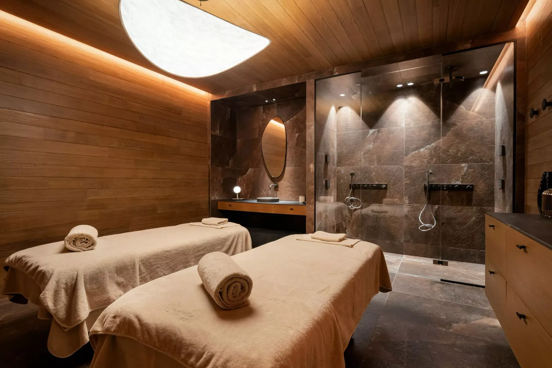 A spa treatment room with two massage tables and a tiled shower area.