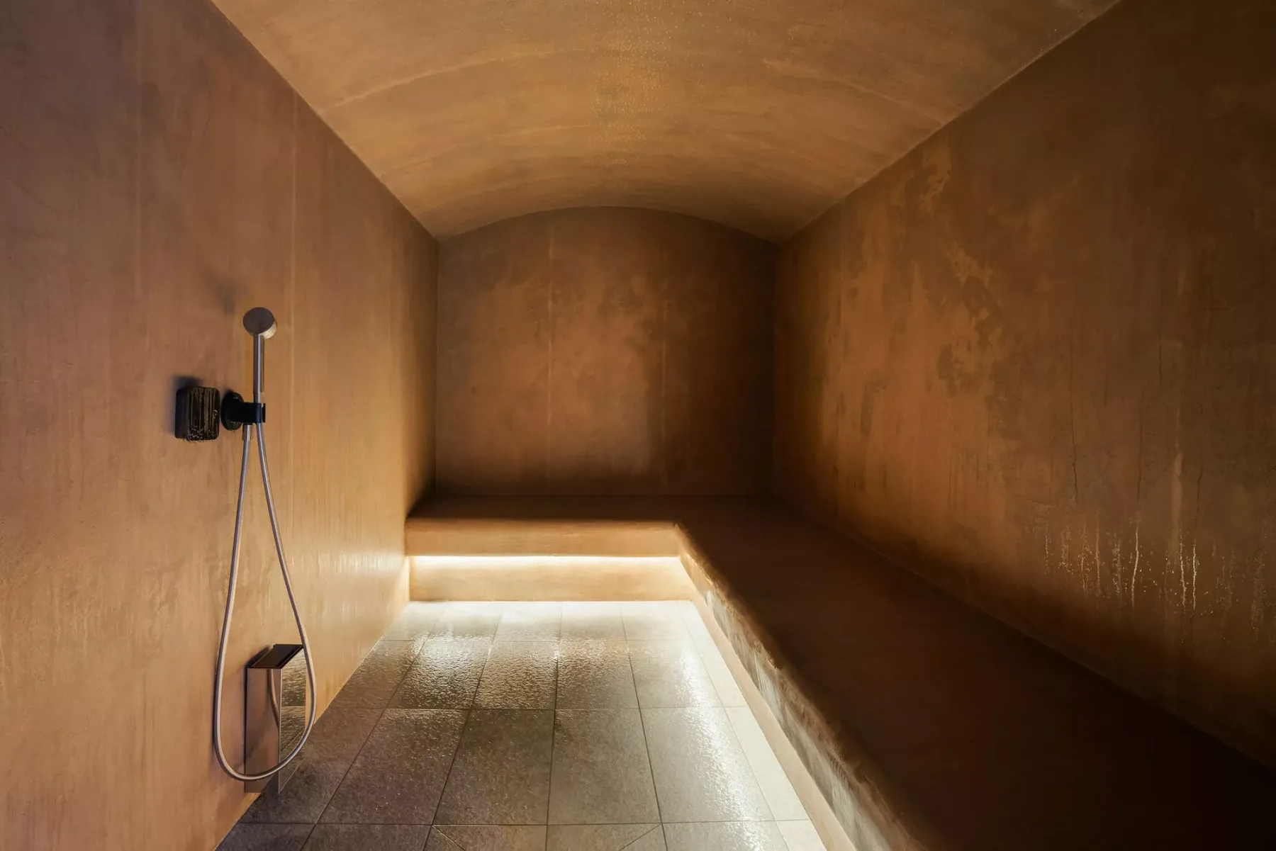 A tiled shower area with warm lighting and bronze-toned walls.