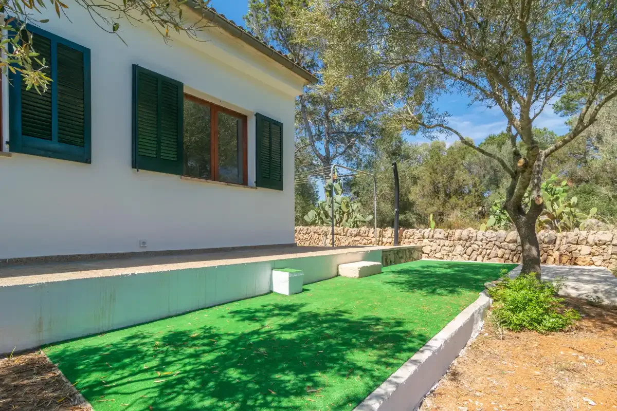 A white house with dark shutters beside a green outdoor lawn.
