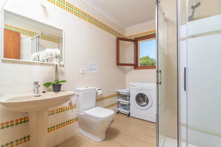 A tiled bathroom with a sink, toilet, washing machine, and shower.