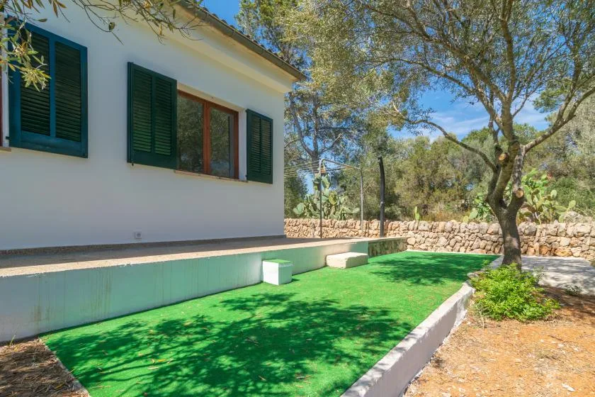 A white house beside a green lawn and a large tree.