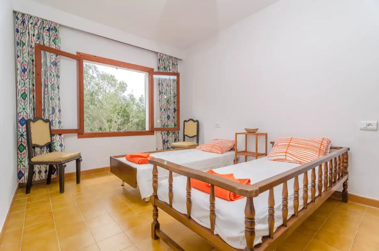 A bedroom with two single beds beside a large window and patterned curtains.