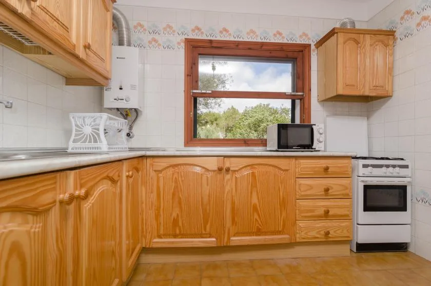 A kitchen with wooden cabinets, a countertop, and a window overlooking greenery.