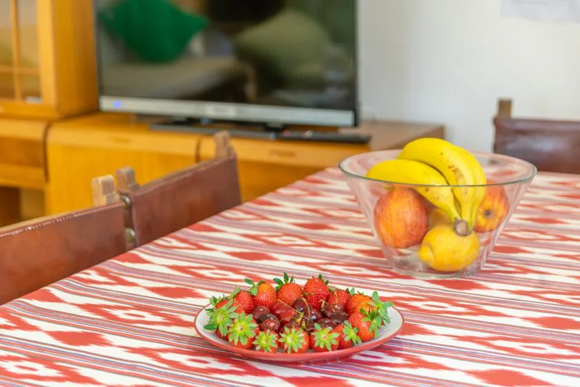 A dining table with bowls of fruit and strawberries sits in front of a television.