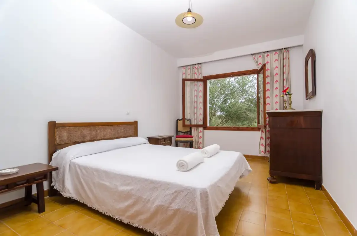 A bedroom with a double bed, a window, and a wooden dresser.