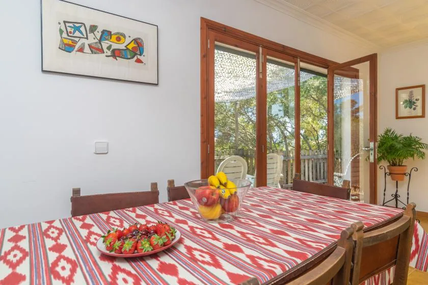 A dining area with a patterned tablecloth and glass doors opening onto a leafy patio.