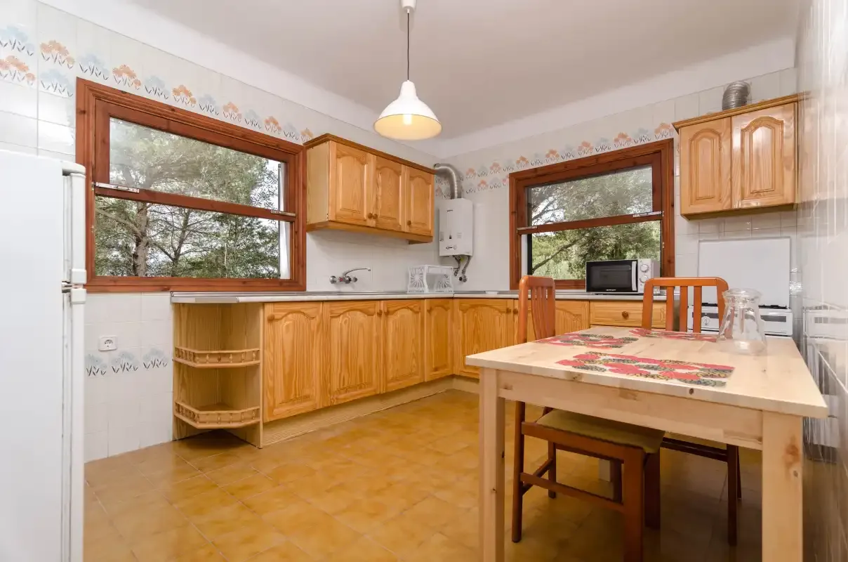 A kitchen with wooden cabinets, a tiled floor, and a dining table.