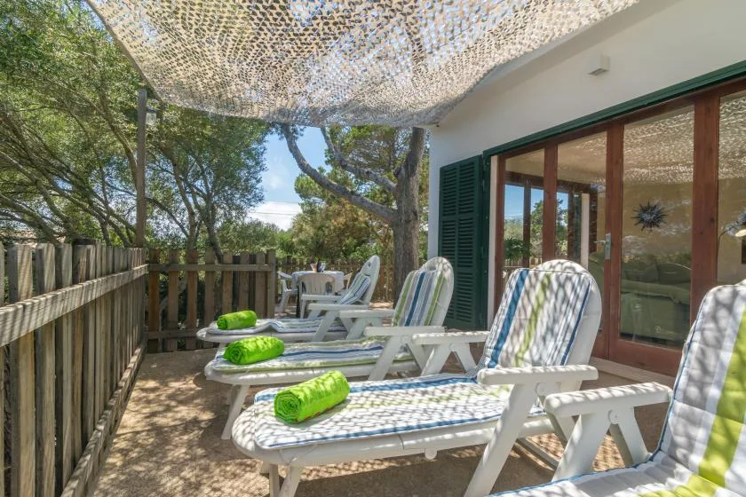 An outdoor patio with cushioned lounge chairs beneath a shade canopy.