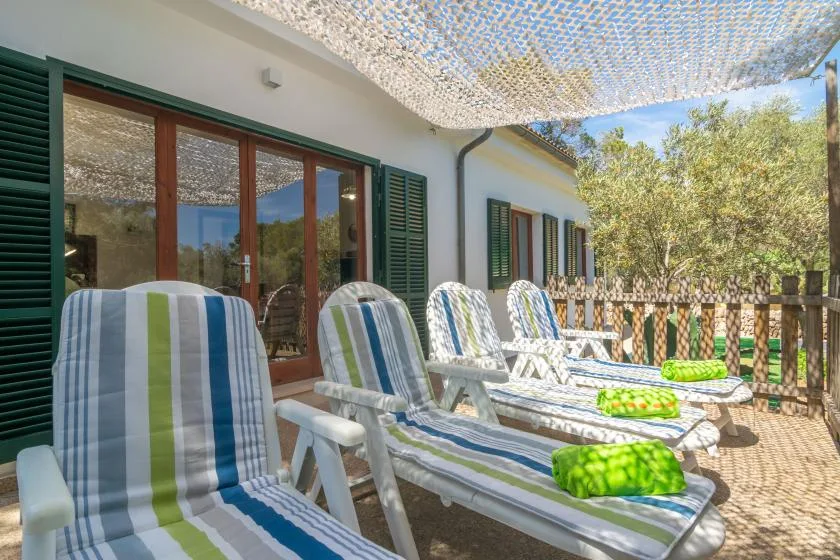 A shaded outdoor patio has striped seating beside windows and a wooden railing.