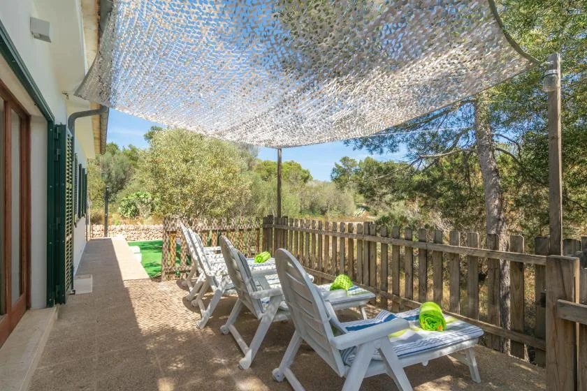 A shaded outdoor deck has reclining seating beside a wooden railing.