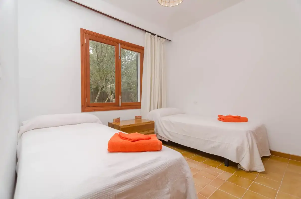 A bedroom with two single beds, a window, and orange towels.