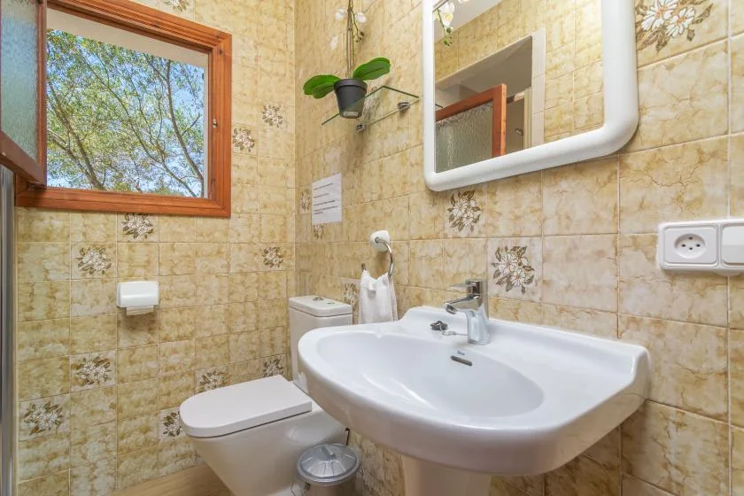 A tiled bathroom with a sink, toilet, and window.