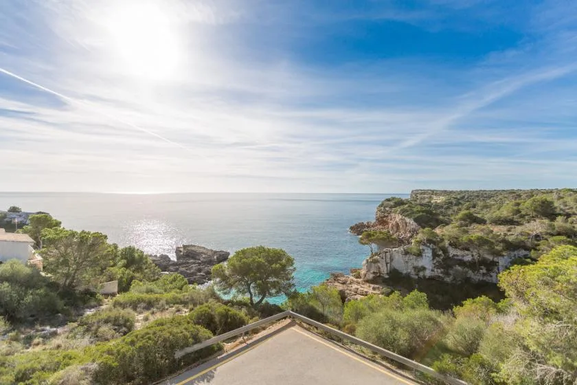 A coastal landscape overlooks calm blue water from a green, rocky shoreline.