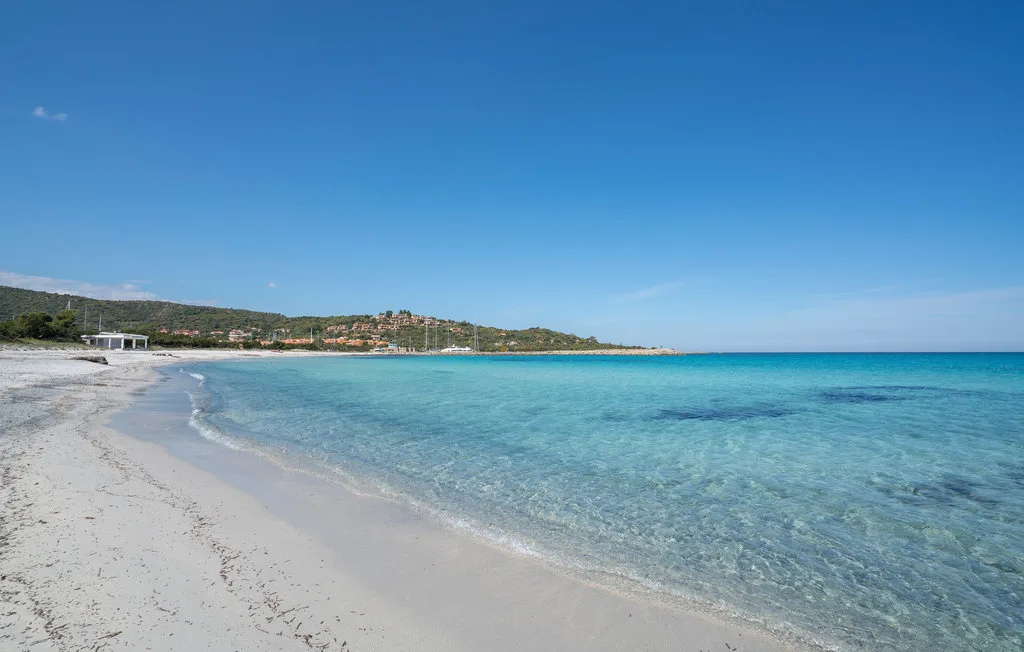 Una playa de arena se curva junto a aguas turquesas y claras bajo un cielo azul.