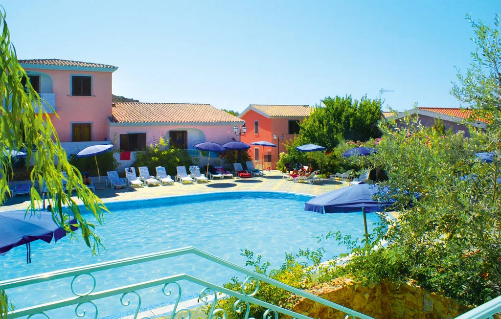 A swimming pool in front of colorful buildings, with lounge seating nearby.