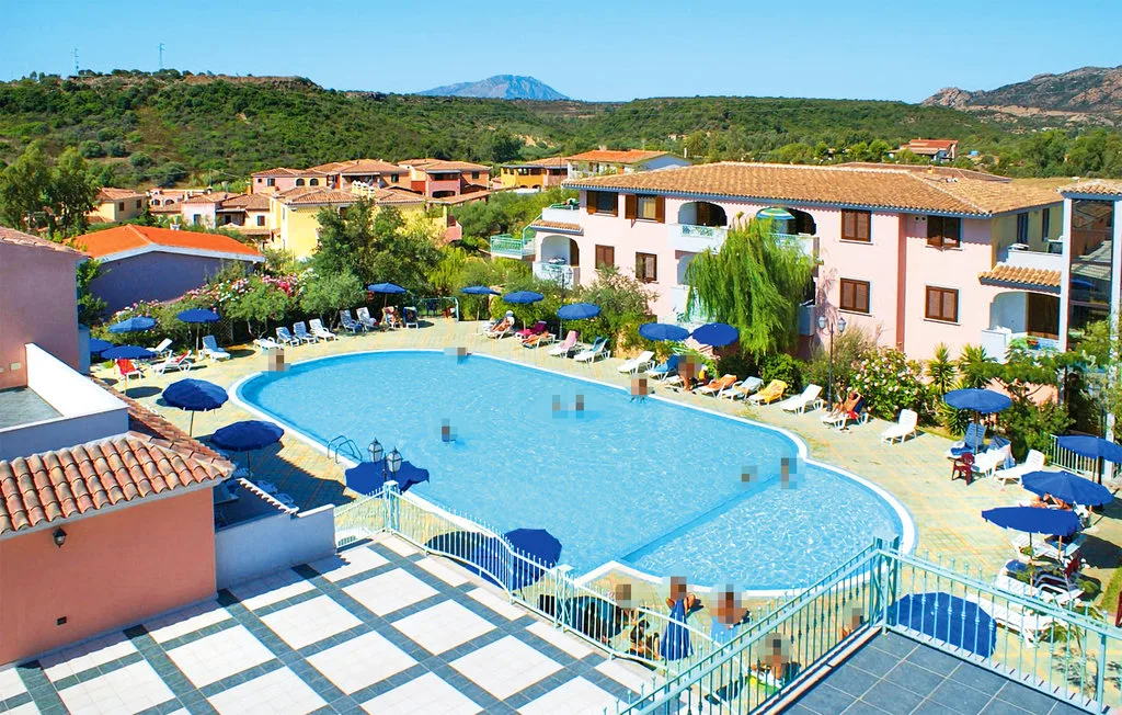 A resort pool beside low-rise buildings, with blue umbrellas around the pool deck.