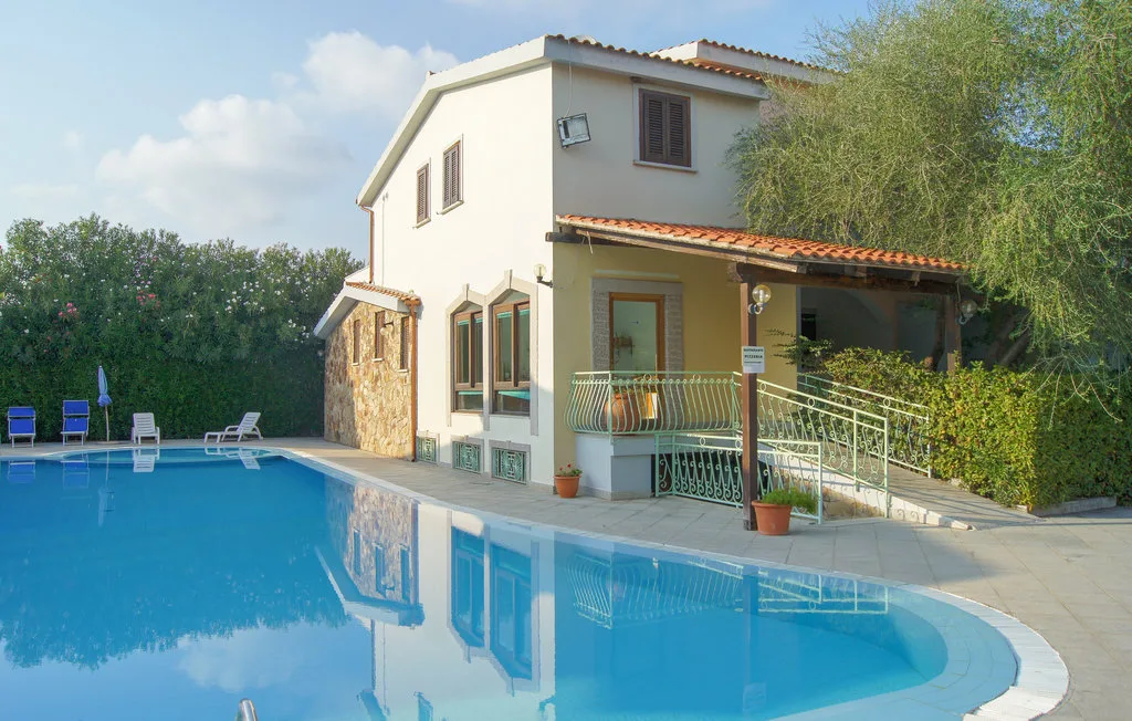 A house beside a swimming pool, with a covered patio and greenery.