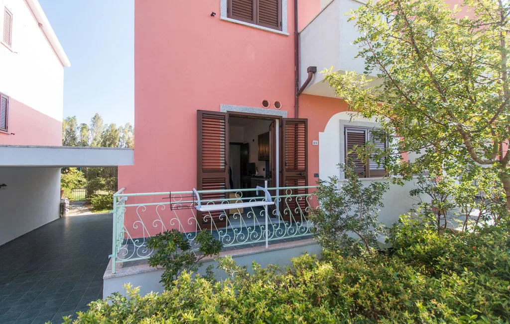 Una fachada rosa con una puerta abierta y un jardín frondoso delante.