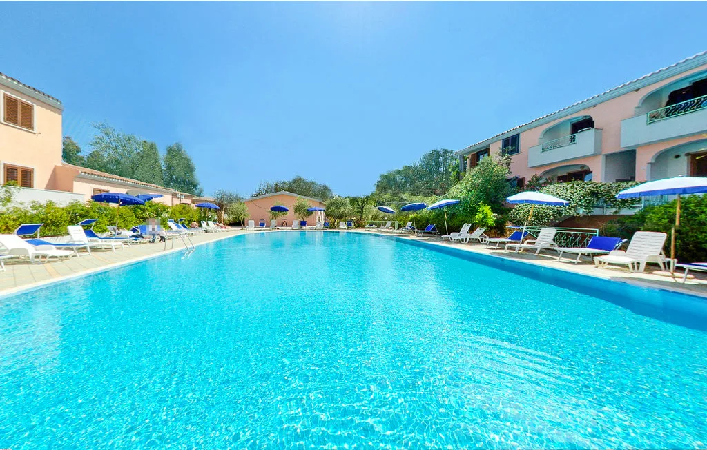 A swimming pool is surrounded by lounge chairs, umbrellas, and buildings.