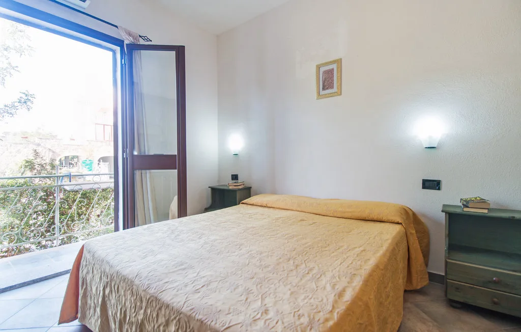 A bedroom with a bed beside an open balcony door.