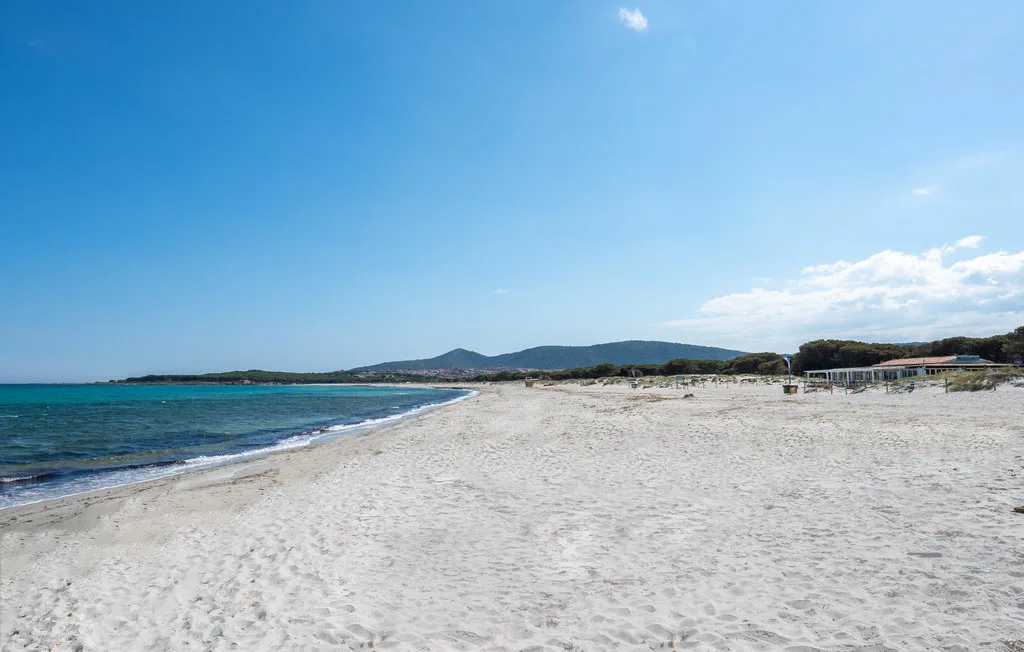A broad sandy beach borders clear turquoise water beneath a blue sky.