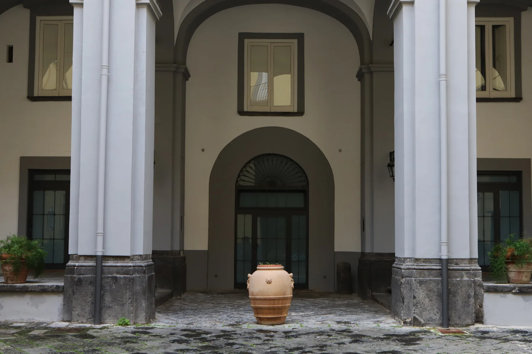 Una entrada de edificio está bajo un pórtico arqueado, con una maceta grande delante.