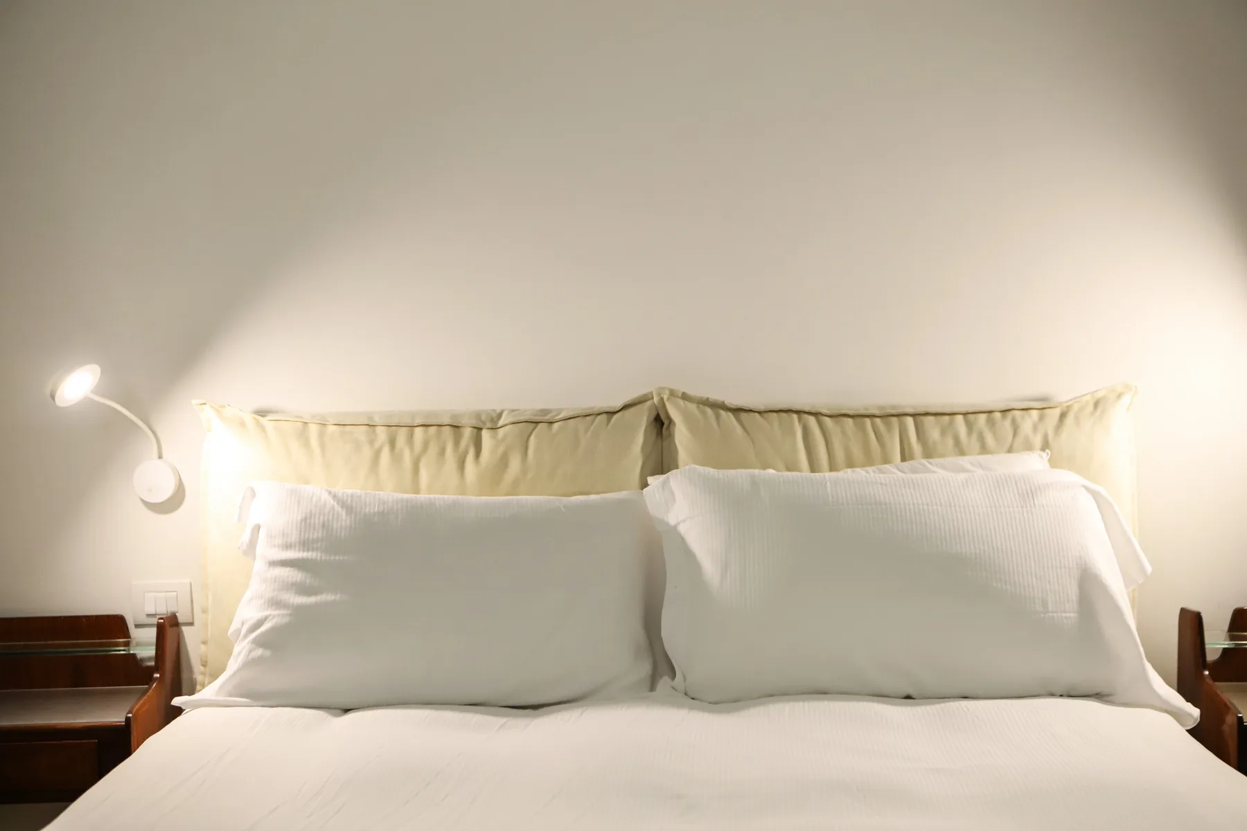 Un dormitorio con una cama tendida y una lámpara de pared encendida.