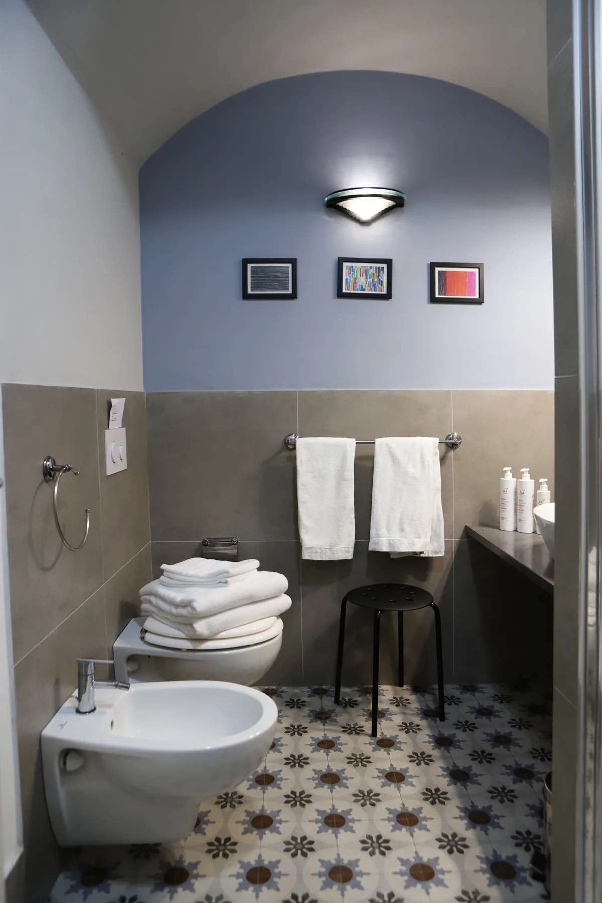 Un baño con suelo de baldosas estampadas, un lavabo de pared y toallas colgadas.