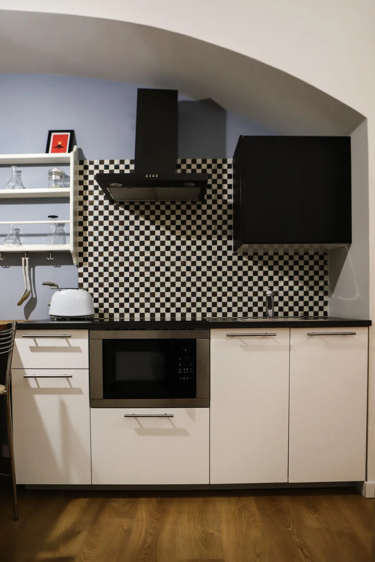 Una cocina compacta con gabinetes blancos, un salpicadero a cuadros y un microondas empotrado.