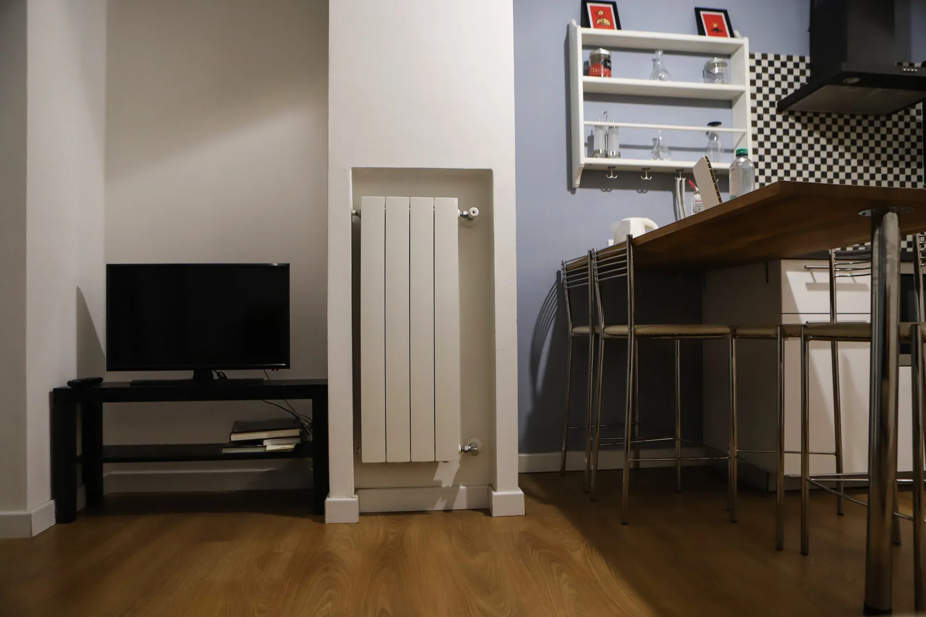 Una sala de estar con un televisor junto a una barra de comedor y taburetes.